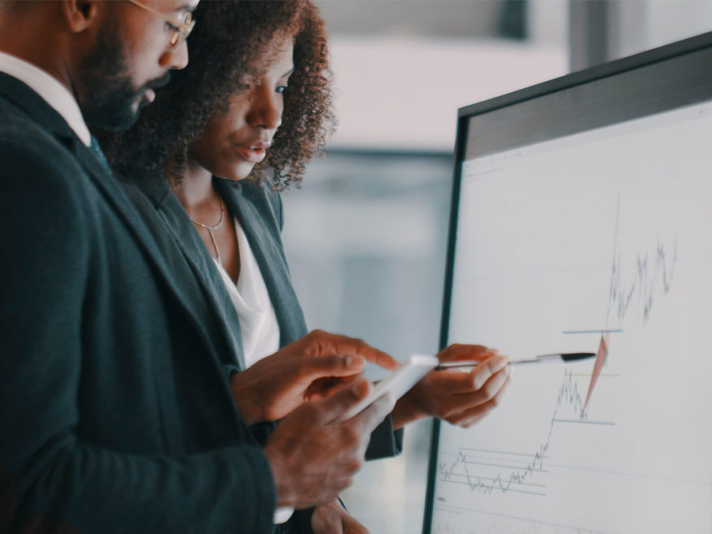 Two people discussing an upward trend graph on a flip chart