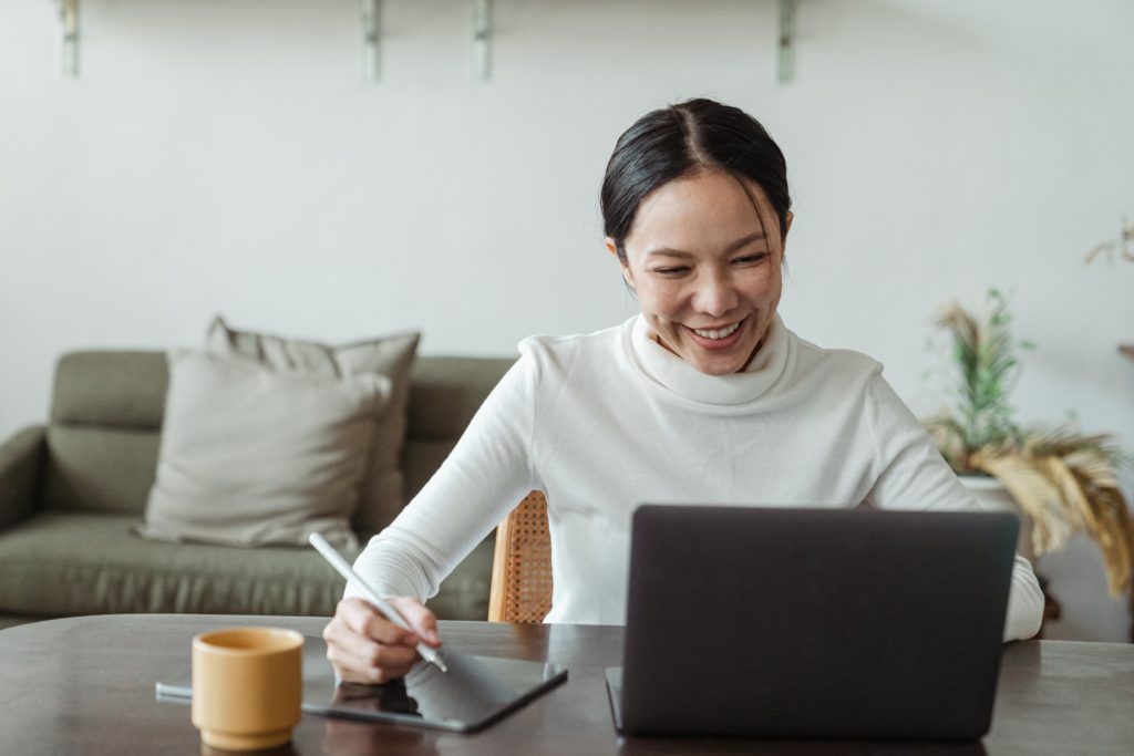 Woman taking notes while viewing laptop