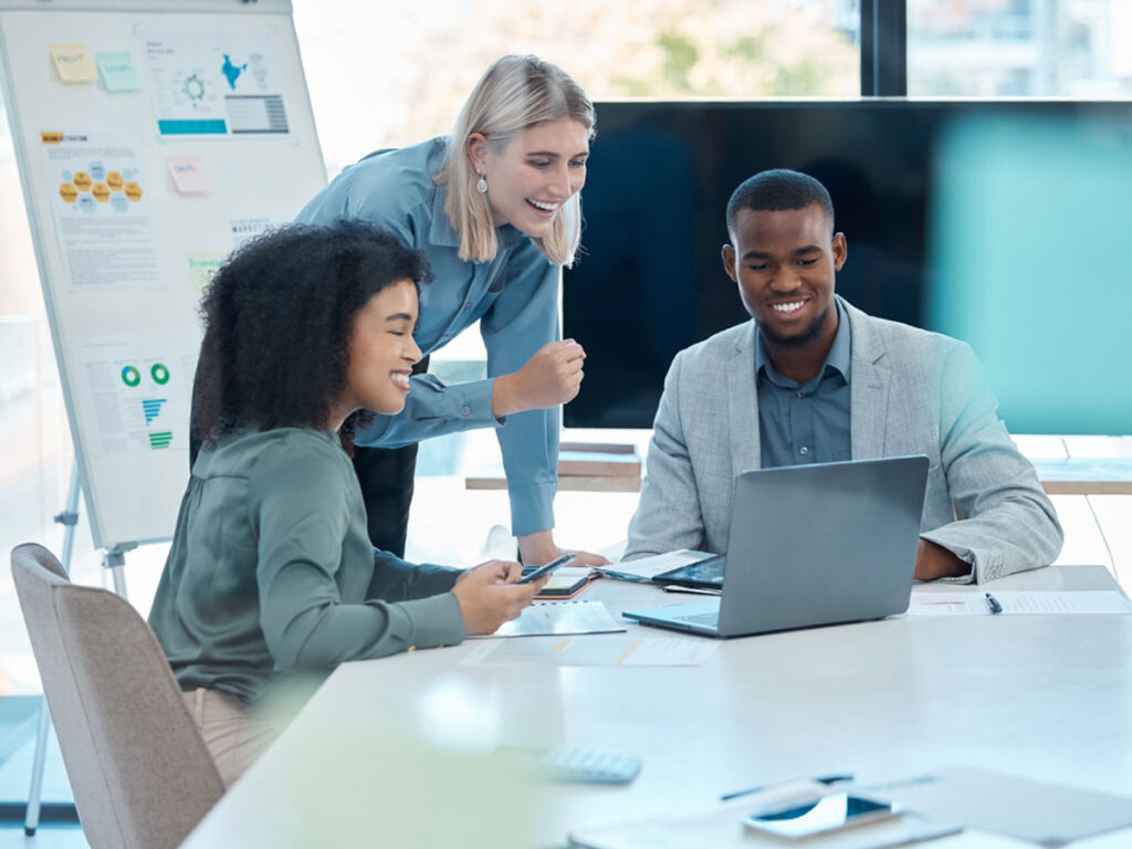 3 office workers gathered around a laptop smiling