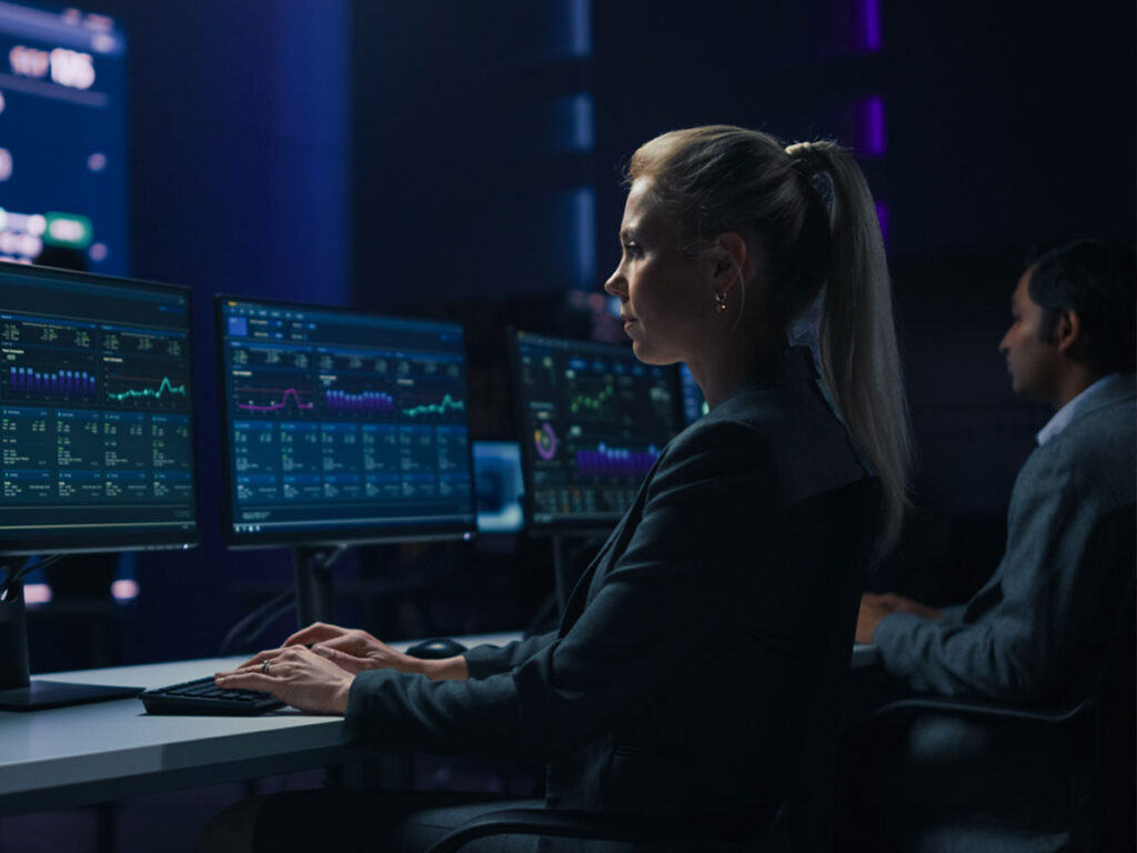 Woman sitting at computer typing in code and monitoring for cybersecurity